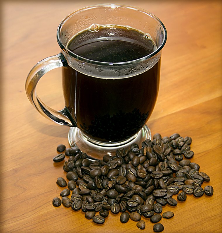 A glass mug of freshly brewed black coffee beside a handful of roasted beans